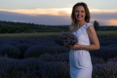 Beyaz elbiseli güzel ve güzel genç bir kadın gün batımında lavanta tarlasında yürüyüş yapmaktan hoşlanıyor. Bulanık arkaplan ile seçmeli odak.