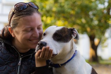 Genç bir kadın, sevgili evcil hayvanı pitbull 'la şehir parkında arkadaşlık etmekten zevk alıyor. Bulanık arkaplanı olan seçici odaklanma. Sığ alan derinliği.