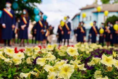 Önünde çiçekler olan bir çiçek tarhı ve mezuniyet gününde mezunlarla dolu bulanık bir arkaplan. Kopyalama alanı için seçici odak arkaplanı