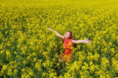 Renkli elbiseli, parlak sarı arka planda, çiçek açan kolza tohumu tarlasında genç, güzel bir kadın. İyi ruh hali kavramı