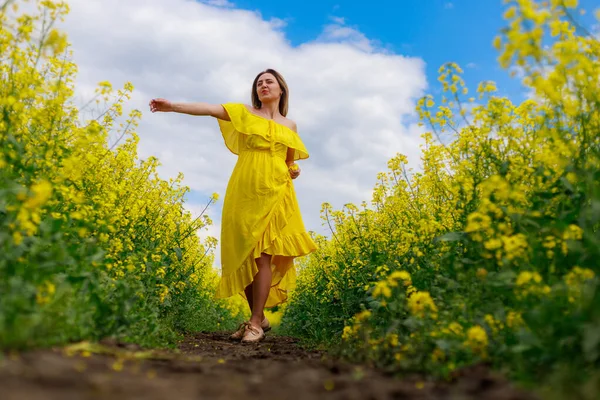 菜の花畑の明るい黄色の背景の雷の上に黄色のドレスの若いかなりの女性 自然との一体性の概念 — ストック写真