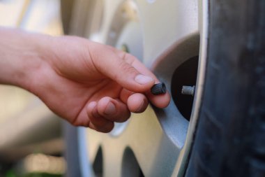 El, arabanın tekerleğindeki meme ucu kapağını büker ya da açar. Havalandırma lastiklerini yerleştirin. Metin veya harf için kopyalama alanı olan tonlanmış arkaplan. Şapkaya odaklan..