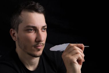 Kaz tüyü giymiş siyah giysili genç yakışıklı bir adam, siyah arka planda gizli bir dart metaforu. Hedef belirleme kavramı