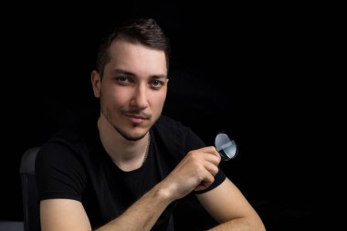 Genç yakışıklı bir adam ve siyah arka planda gösterişsiz bir büyüteç. Arama sembolü. Soruşturma kavramı