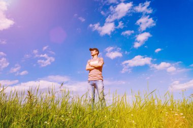 Güzel bir gökyüzünün ve yeşil bir arazinin arka planında yakışıklı bir adam coşkuyla mesafeye bakıyor. Kopyalama alanı olan arkaplan