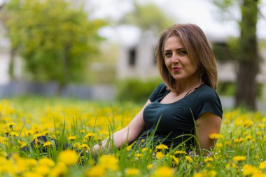 Karahindiba çiçekleri açarken bir şehir parkında genç bir kadın. Sarı neşeli şimşek konsepti. Mutluluk ve özgürlüğün sembolü