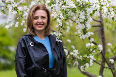 Otuz yaşından büyük mutlu bir kadının portresi çiçek açan ağaçların bulanık arka planında. Metin için kopyalama alanı