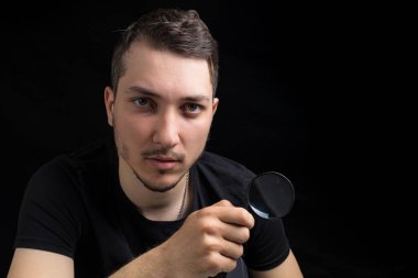 Genç yakışıklı bir adam ve siyah arka planda gösterişsiz bir büyüteç. Arama sembolü. Soruşturma kavramı