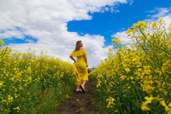 菜の花畑の明るい黄色の背景の雷の上に黄色のドレスの若いかなりの女性 自由の概念 — ストック写真