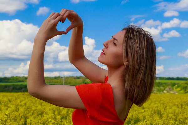 Young pretty woman in colored dress on lightning cheerful yellow background of blooming rapeseed field. Good mood concept