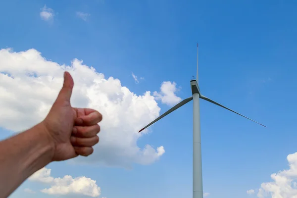 Windmills for electricity generation. Green energy concept. Background with copy space for text. Thumbs up gesture on blurred foreground.