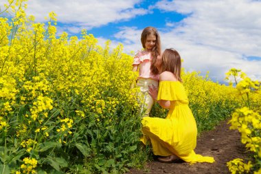 Anne ve kızı açık hava yaşam tarzında. Arka planda çiçek açan kolza tohumu tarlasının neşeli sarı rengi. Çocuk sevgisi kavramı.