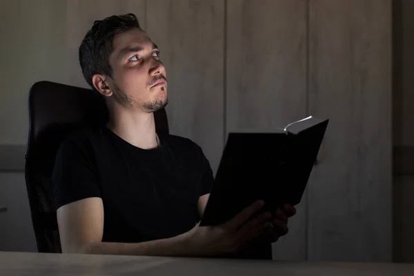 暗闇の中でハンサムな男か大人の男が輝く本を読みます 教えることは闇ではなく光です — ストック写真