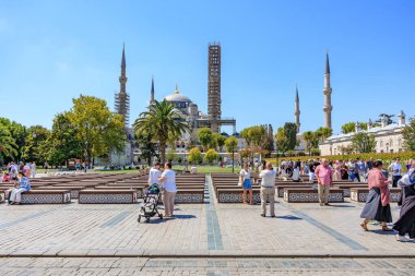 Tourists in busy plaza near historic mosque with towers and palms on sunny day. August 12, 2025 Istanbul Turkey.