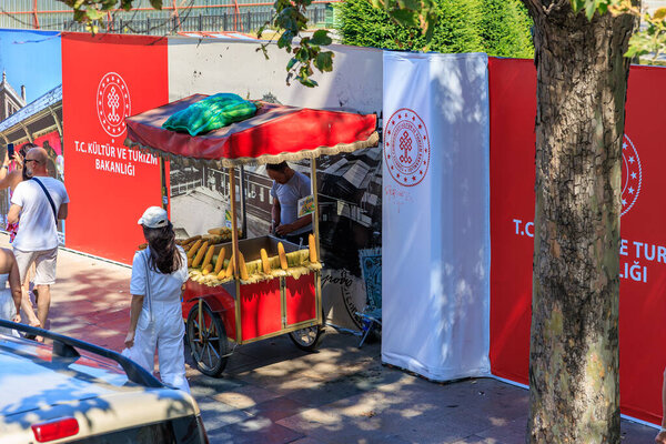 Street vendor in white shirt selling corn from red cart in urban setting. August 12, 2025 Istanbul Turkey.