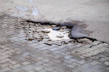 Damaged paved road with pothole and water accumulation.