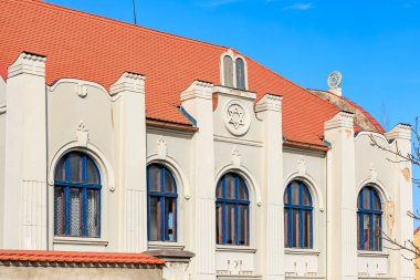 Historic synagogue with red roof and arched windows against blue sky.