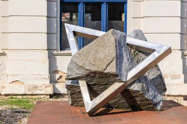 Abstract stone sculpture with metallic frame near historic building.. March 22, 2025, Kutna Hora, Czech Republic.