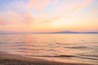 Gökyüzü güzel pembe bir renk ve okyanus sakin. Güneş batıyor, huzurlu bir atmosfer yaratıyor.