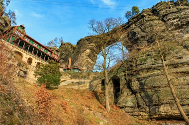 Natural rock arch in european mountain landscape with historic building and winter trees.