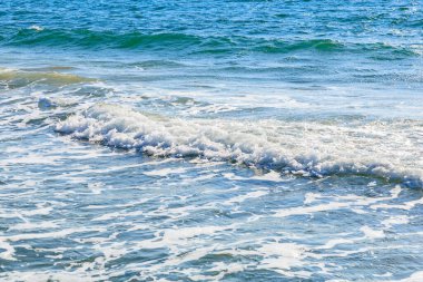 Ocean waves gently crashing on a sunny beach shoreline.