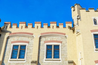 Medieval castle facade with stone battlements and blue sky.