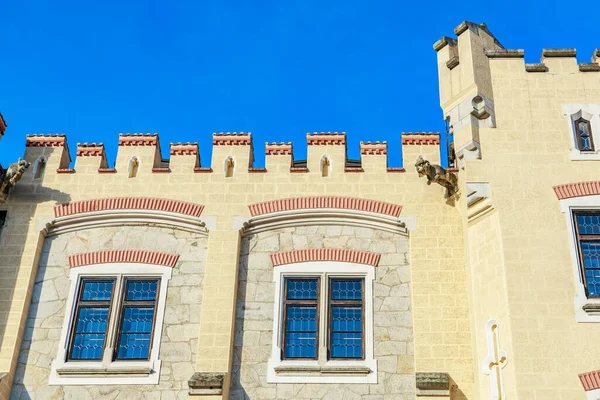 Medieval castle facade with stone battlements and blue sky.