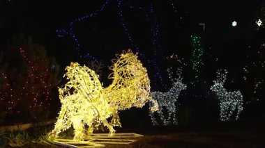 Kış parkında Noel kutlaması sırasında altın LED ışıklarıyla parlayan bir ren geyiğinin dekoratif aydınlatılmış heykeli..