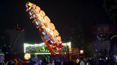Dinamik lunapark eğlencesi, parlayan neon ışıklarıyla dönüyor ve ziyaretçiler Noel fuarında neşeli atmosferin keyfini çıkarıyorlar. 20 Aralık 2024 Balti Moldova.