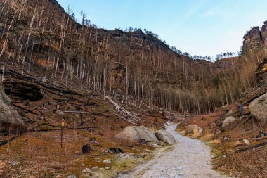 Scenic pathway through rocky landscape with bare trees in mountain valley.
