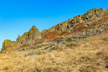 Basalt columns in scenic landscape with clear blue sky.