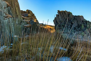 Basalt columns and vegetation in rocky landscape under clear blue sky.