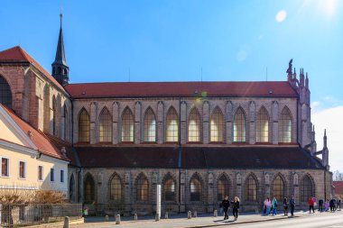 Güneşli bir günde, kırmızı çatılı ve yürüyen insanlarla dolu Gotik Kilisesi 22 Mart 2025, Kutna Hora, Çek Cumhuriyeti.