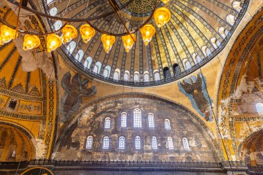 Süslü kubbe ve aydınlatılmış avizelerle tarihi Bizans mimarisinin iç görünümü.