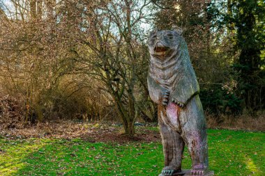 Ormanda yeşil çimenler ve yapraksız ağaçlarla süslenmiş ayı heykeli. 17 Mart 2025, Konopiste Şatosu, Çek Cumhuriyeti.