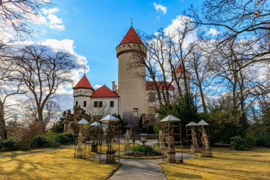 Mavi gökyüzünün altında ağaçlarla ve bahçelerle çevrili bir ortaçağ kalesi. 17 Mart 2025, Konopiste Şatosu, Çek Cumhuriyeti.