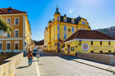 Tarihi mimarinin ve kaldırım taşlarında gezinen bir kadının yer aldığı madalyonlu güneşli bir gün. 18 Mart 2025, Madalyon, Çek Cumhuriyeti.