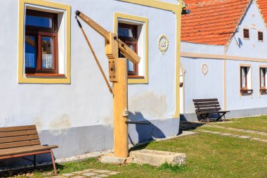 Geleneksel su kuyusu ve renkli evlerle büyüleyici köy manzarası. 21 Mart 2025, Holasovice, Çek.