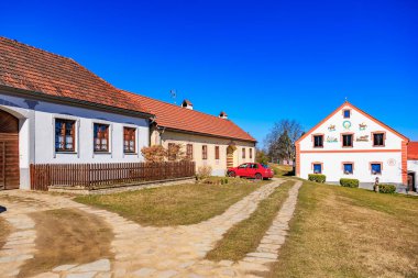 Tarihi kır evi, taş patika ve parlak mavi gökyüzü ile taşralı köy manzarası. 21 Mart 2025, Holasovice, Çek.