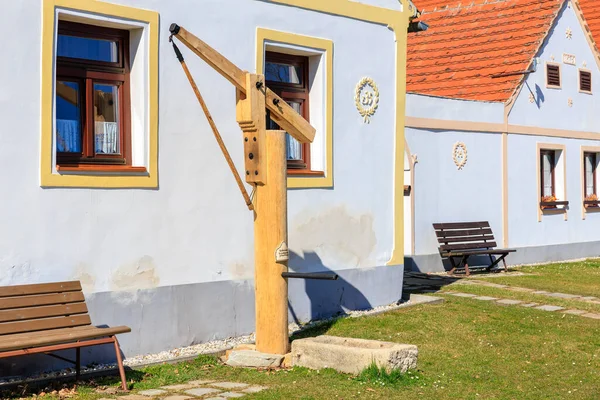 Geleneksel su kuyusu ve renkli evlerle büyüleyici köy manzarası. 21 Mart 2025, Holasovice, Çek.