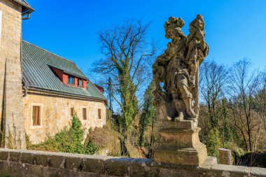 Tarihi taş heykel ve kırsal alanda kırsal bir bina. 16 Mart 2025, Hruba Skala Şatosu, Çek Cumhuriyeti.