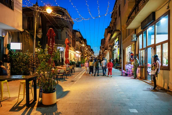 Farklı insanlar ve açık kafelerle aydınlık bir kaldırım taşı caddesinde akşam yürüyüşü. 3 Mayıs 2025 Romanya.