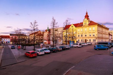 Günbatımında tarihi binalar ve park halindeki arabalarla şehir meydanı. 17 Mart 2025, Benesov, Çek Cumhuriyeti.