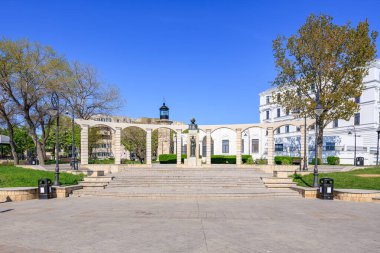 Taş kemerleri ve açık mavi gökyüzünün altında yeşil park manzarası olan tarihi bir anıt. 3 Mayıs 2025 Romanya.