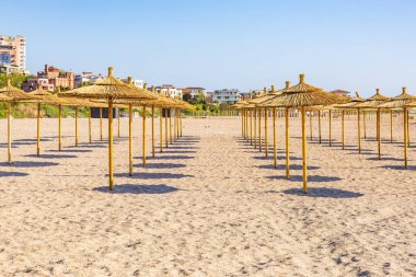 Kumlu sahil şeridinde saman şemsiyeli güneşli sahil.