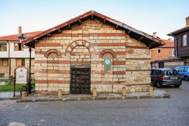 Eski Avrupa kasabasında kemerli camları ve kırmızı tuğlalı detayları olan tarihi taş kilise. 1 Ağustos 2025, Nessebar Bulgaristan.
