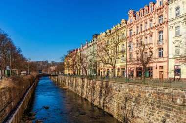 Karlovy Cumhuriyeti 'nde nehir boyunca uzanan renkli tarihi binalar var. 18 Mart 2025, Karlovy Vary, Çek Cumhuriyeti.
