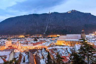 Geceleri arka planda büyük bir kilise olan bir şehir. Yerdeki kar ve binalardaki ışıklar huzurlu ve huzurlu bir atmosfer yaratıyor. 14 Aralık 2024 Brasov Romanya