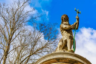 Antik Neptün heykeli canlı mavi gökyüzünün altında çıplak ağaçlarla birlikte. 17 Mart 2025, Konopiste Şatosu, Çek Cumhuriyeti.