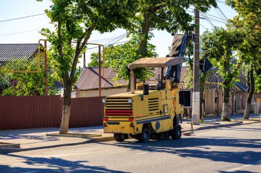 Banliyö caddesinde ağaçlarla kaplı sarı asfalt değirmen makinesi.